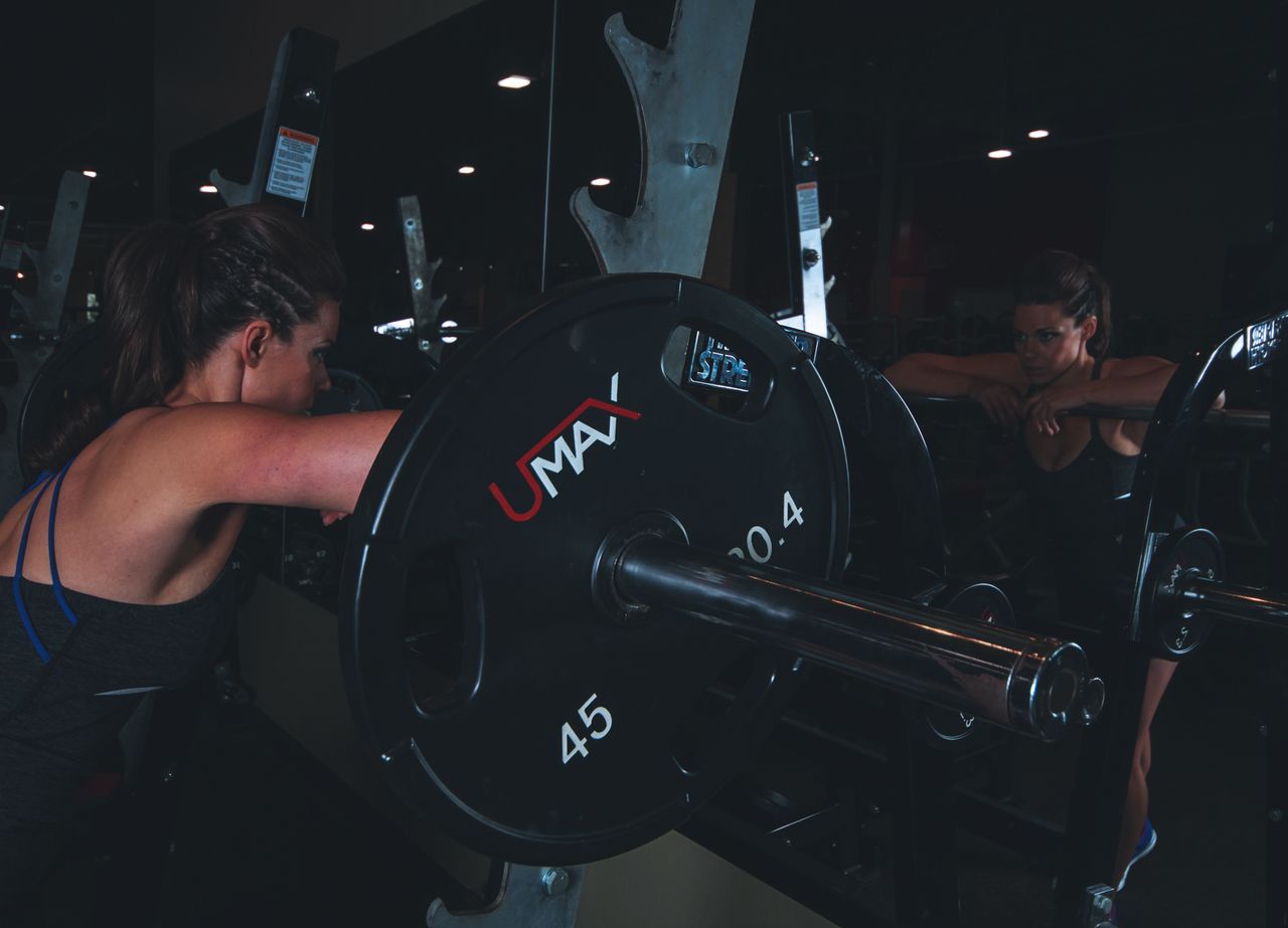 Woman in gym attire reflects in mirror while preparing for weightlifting session.