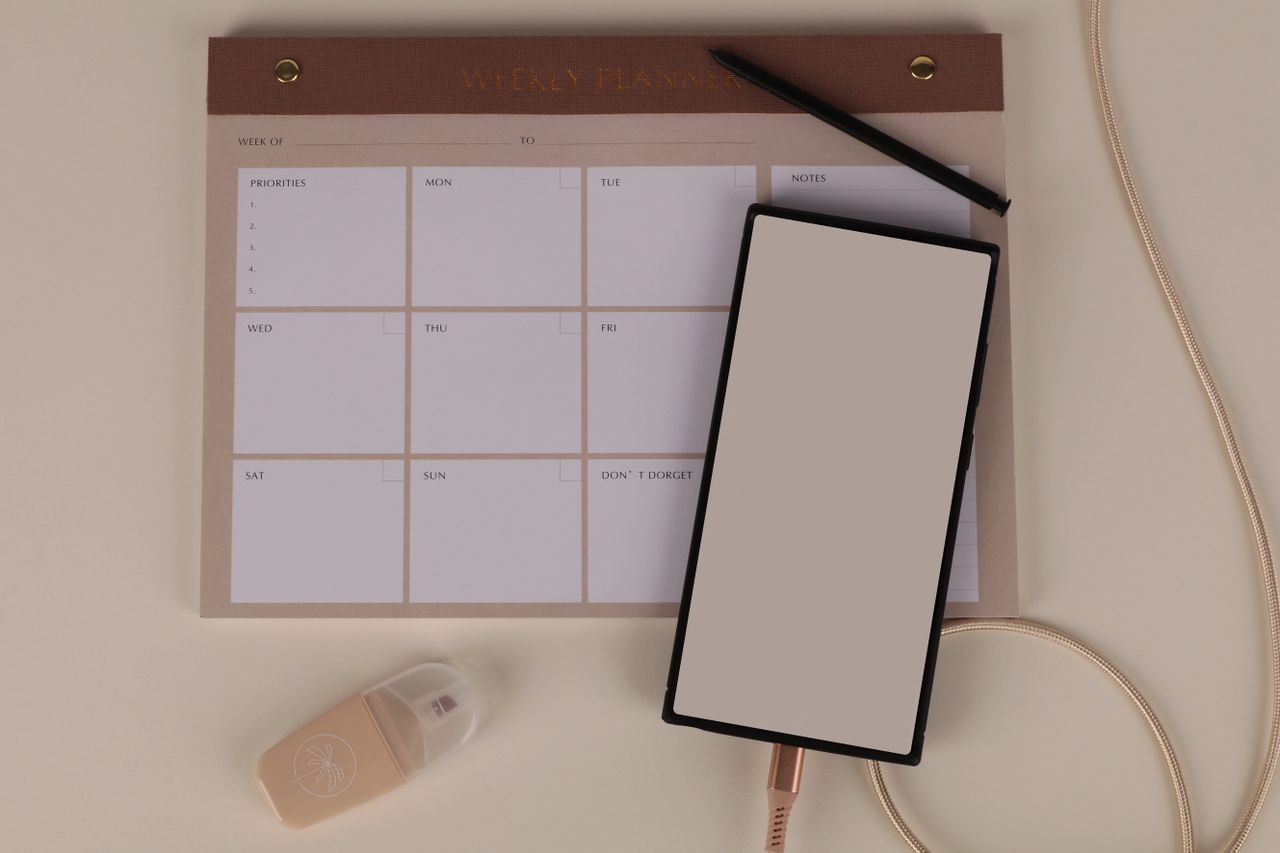 Flat lay of a minimalist desk setup featuring a weekly planner, smartphone, and stationery.