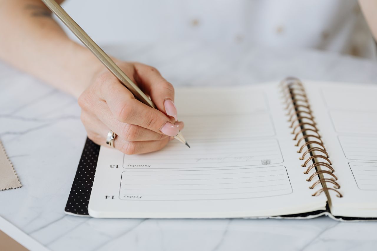 Crafting Captivating Headlines: Your awesome post title goes here Close-up of a woman's hand writing in a spiral notebook on a marble desk.